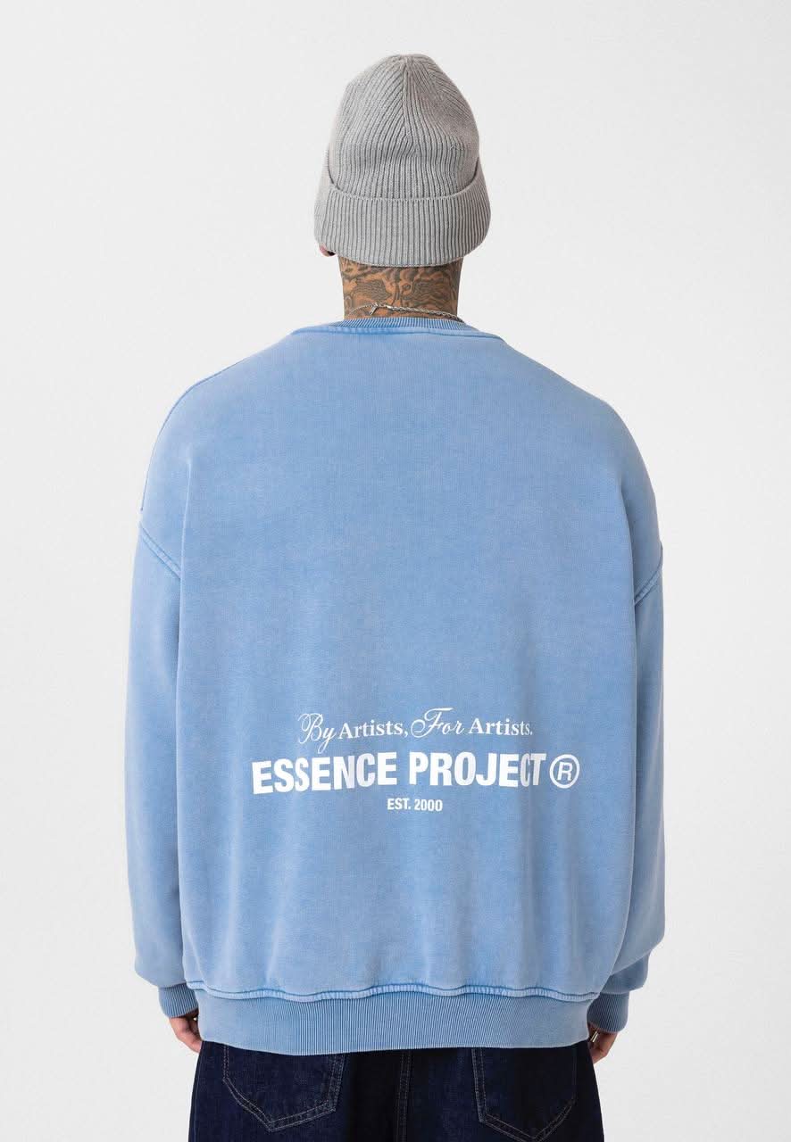 Person wearing a blue sweatshirt with 'Essence Project' logo on the back, standing against a white background